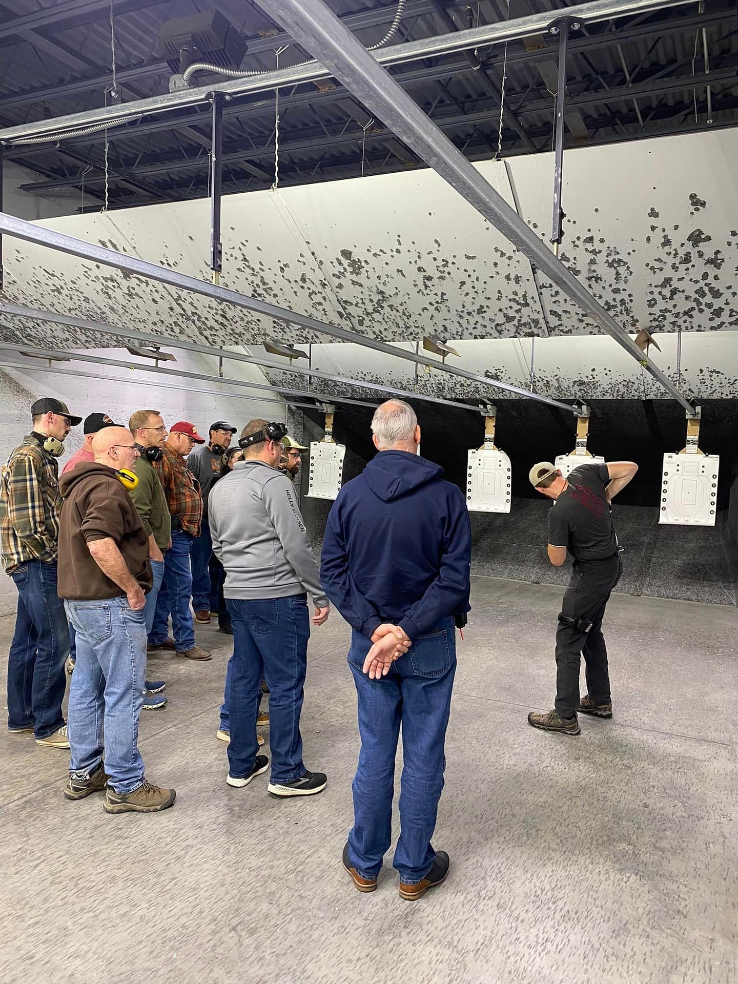 a man demonstrating Holstering techniques in an indoor range to a class of 10 student